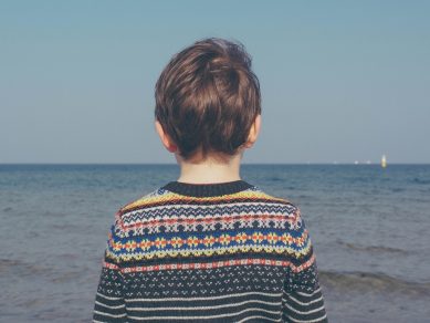 Young child with their back to the camera, looking out to sea